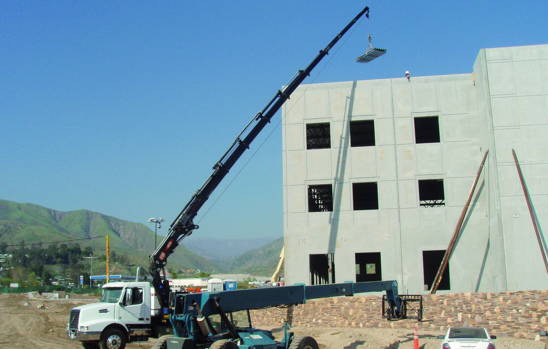 PM knuckle boom crane lifting materials at a construction site